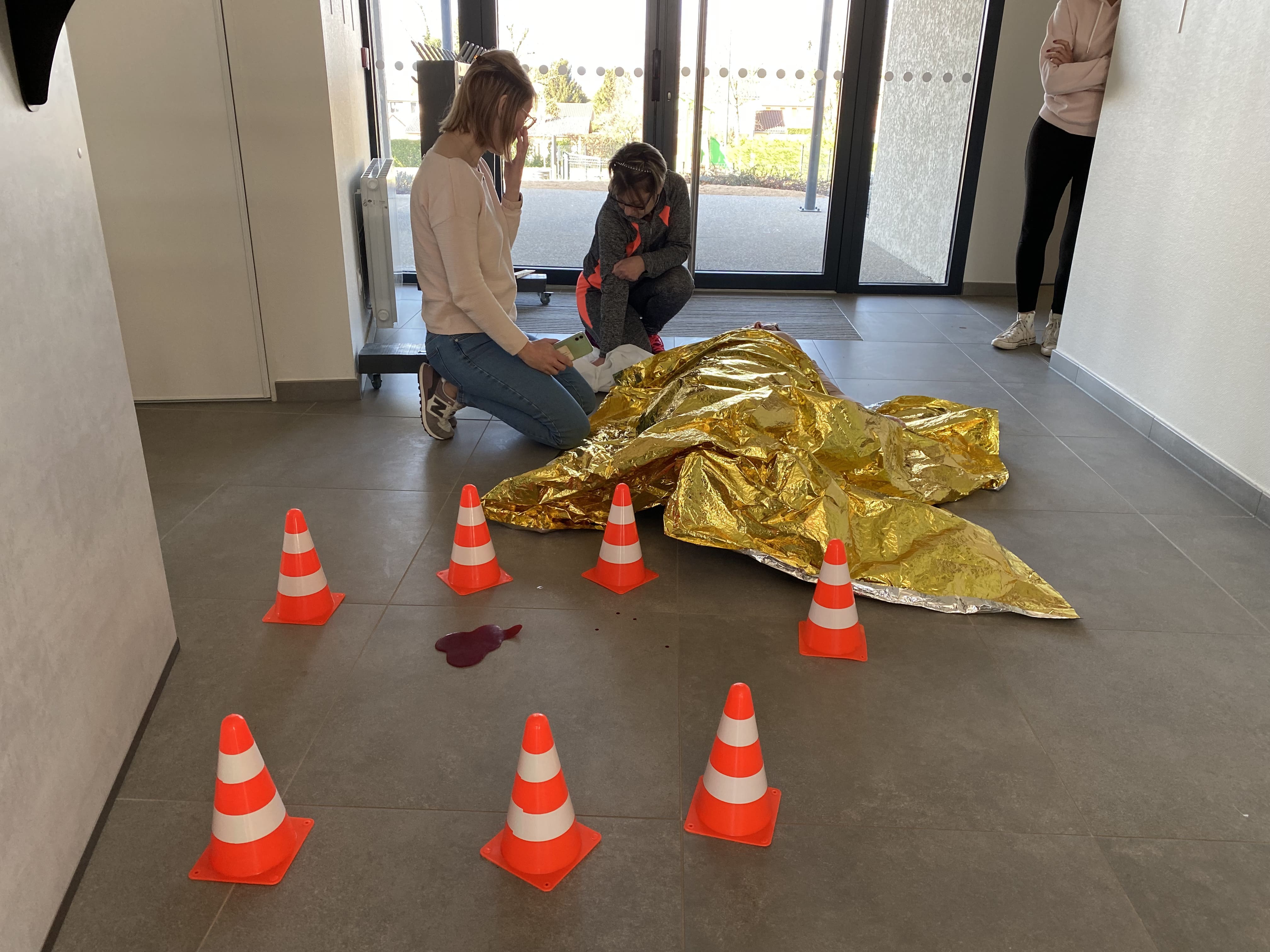 formation-AFGSU-couverture-survie Deux personnes s'occupent d'une couverture de survie dorée.